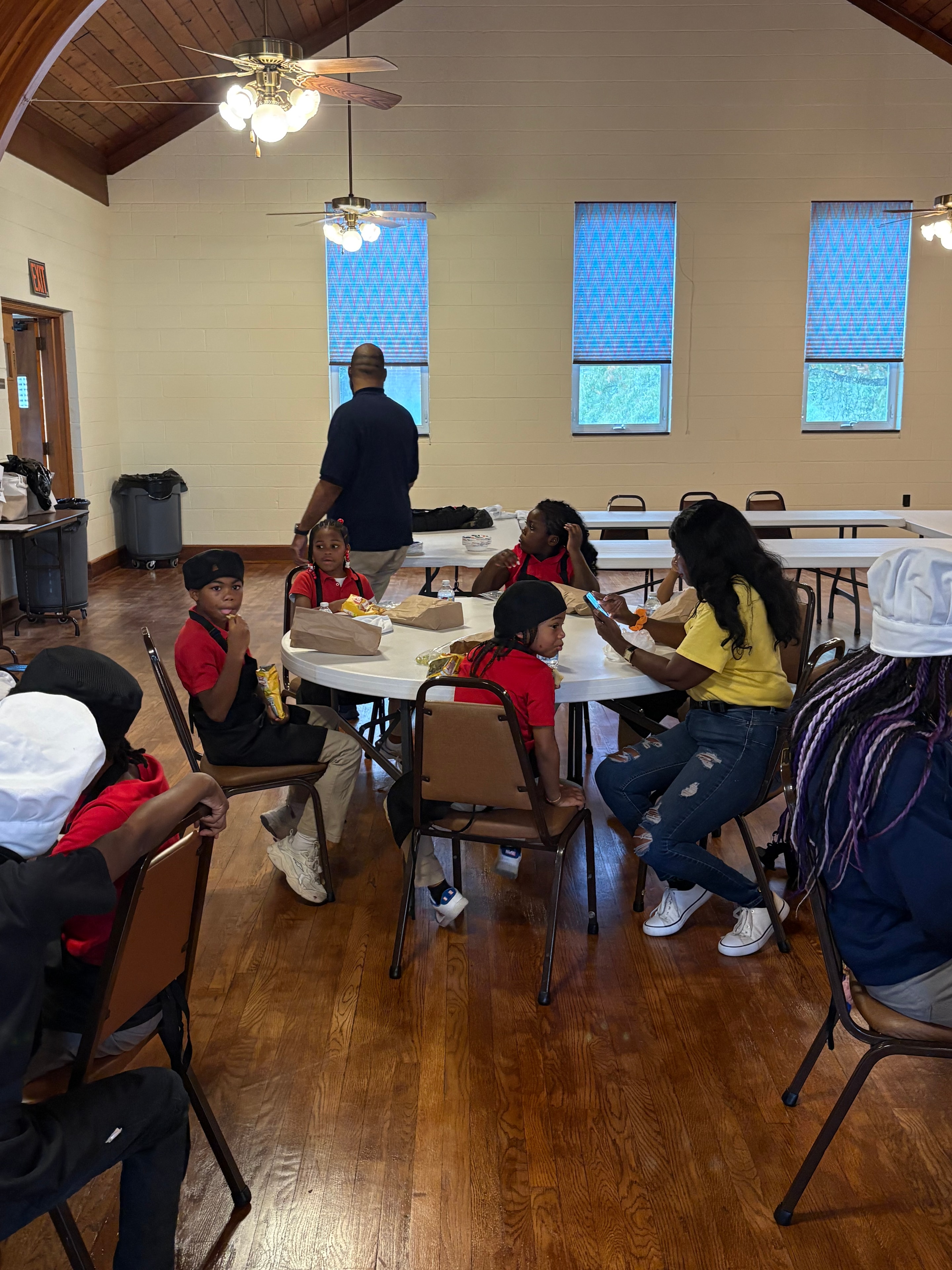 Children in red shirts working alongside adults at tables during a Kids R Cookin' session
