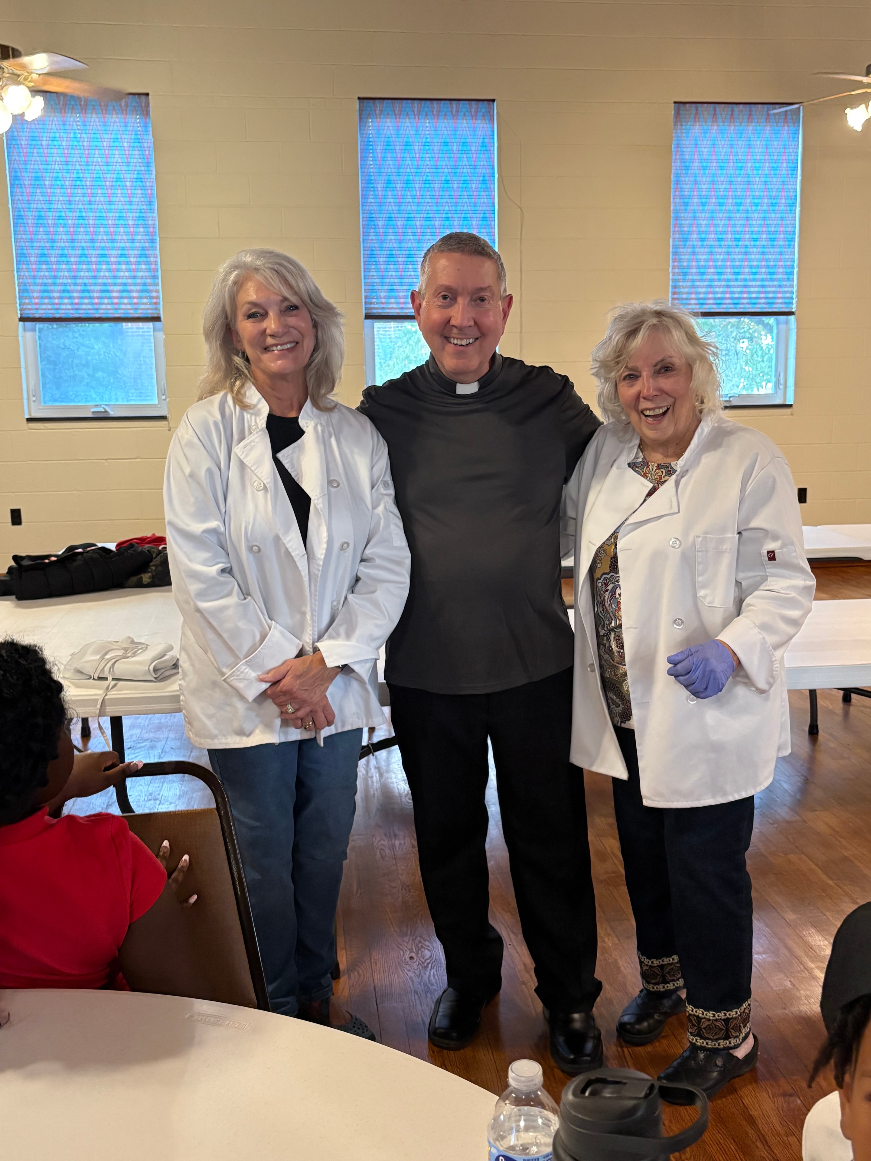 Fr. Jack with two volunteers in white chef coats at a Kids R Cookin' session